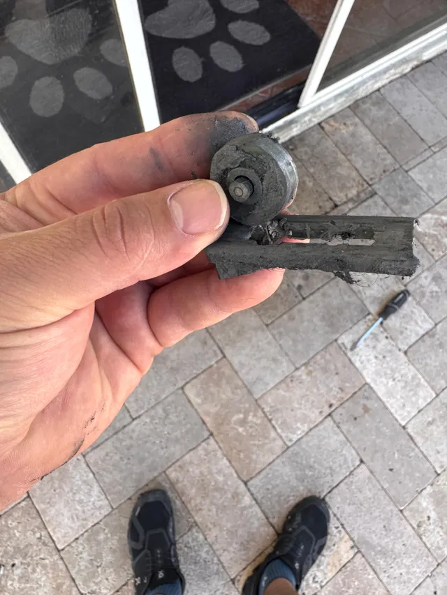 A hand holding a removed metal sliding door roller assembly